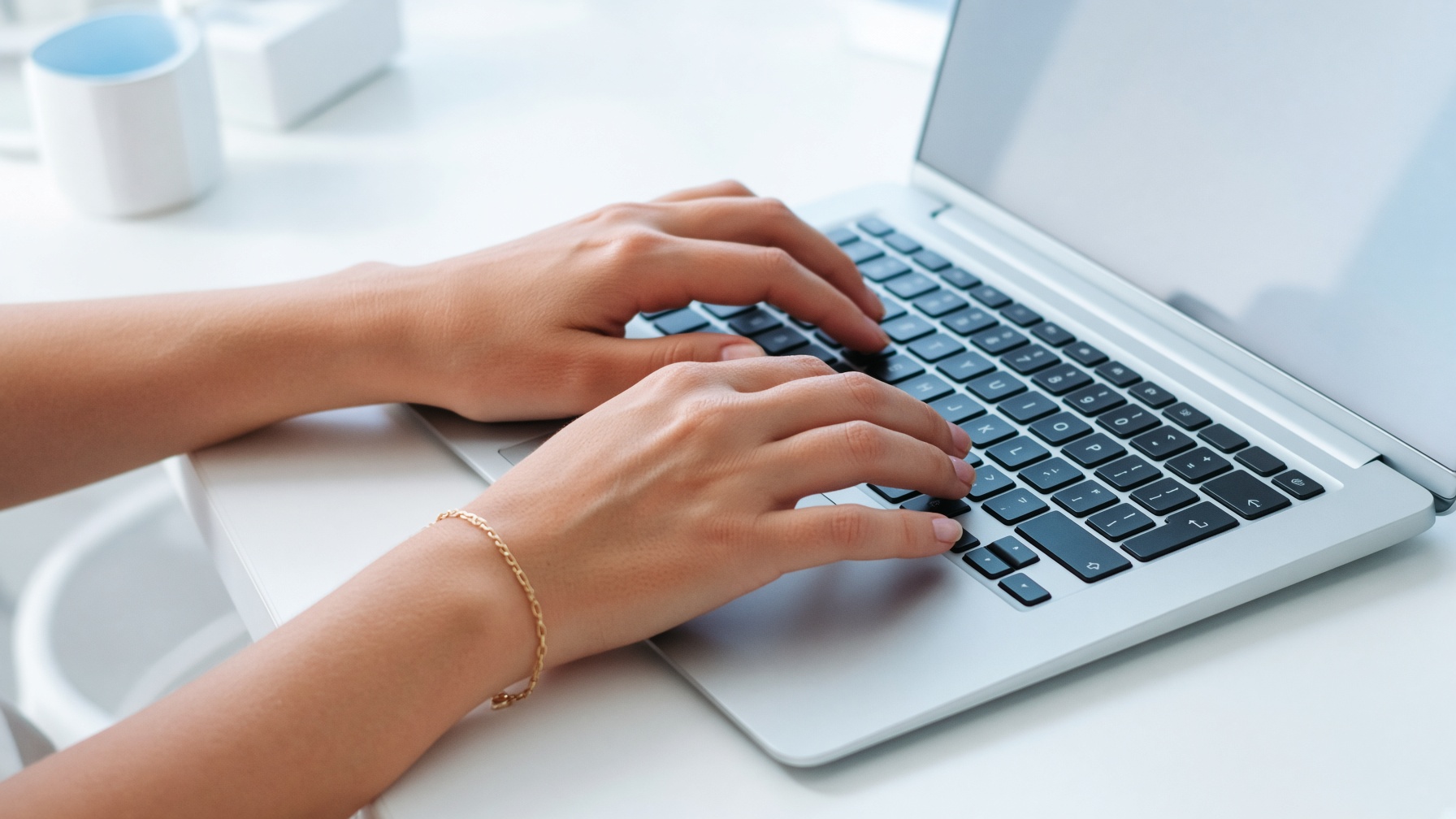 Hands typing on a laptop, cropped at the forearms